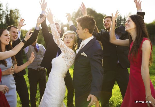 Full length portrait of newlywed couple dancing and having fun with bridesmaids and groomsmen in green sunny park