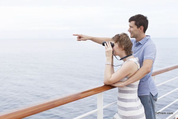 couple enjoying cruise, woman looking through binoculars and man showing something ahead